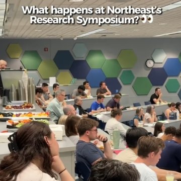 A crowded lecture hall filled with students and faculty seated at tiered rows of tables with food, beneath a wall decorated with colorful hexagonal panels in green, blue, and yellow. Text overlay reads: 'What happens at Northeast's Research Symposium? 