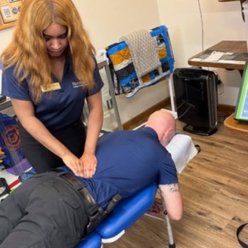 A Northeast College student in a navy polo performing a back treatment on a patient lying on a blue massage table.