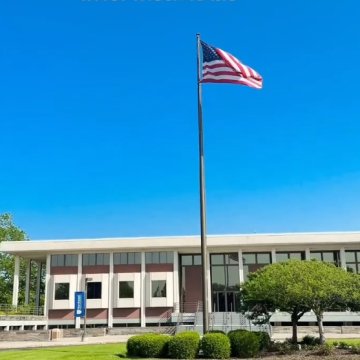 An American flag flying in front of a Northeast College of Health Sciences building on a clear blue-sky day, with text reading "Red, White & #NortheastBlue."