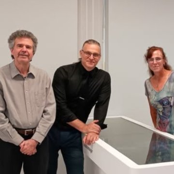 Three faculty or staff members posing beside a digital anatomy table in a new lab space.