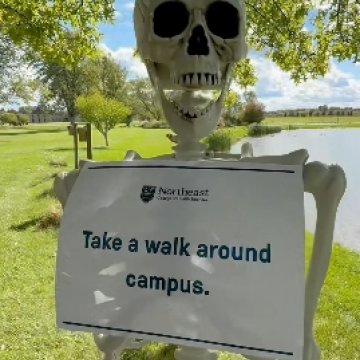A plastic skeleton outdoors holding a Northeast College sign reading “Take a walk around campus.”