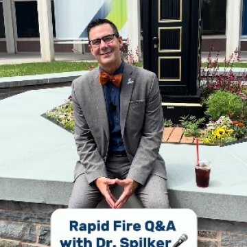 A man in a gray suit and orange bow tie seated outside a Northeast College building, with text reading “Rapid Fire Q&A with Dr. Spilker.”