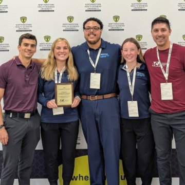 Five people posing with an award plaque in front of a Northwestern Health Sciences University backdrop at a conference.