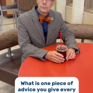 A man in a gray suit and orange bow tie seated inside, with text reading “what is one piece of advice you give every student?"